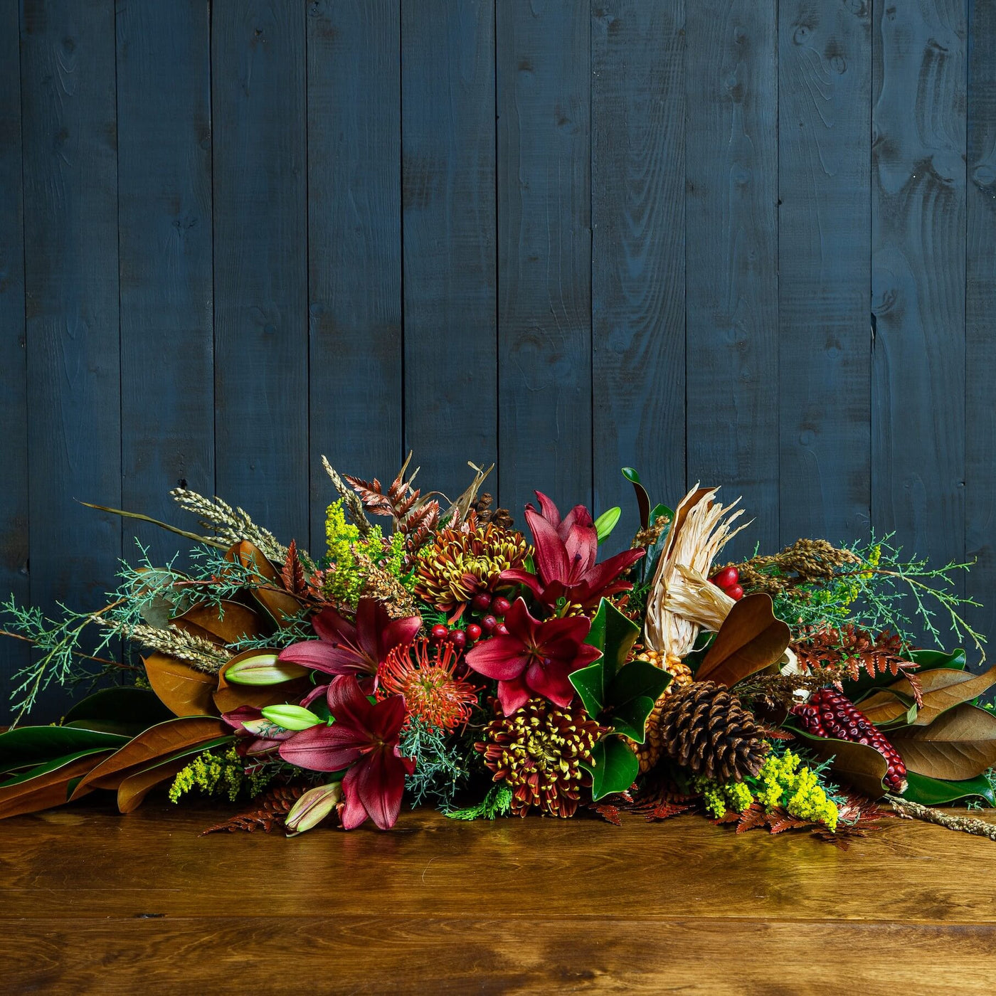 Rustic autumn floral centerpiece with red lilies, pinecones, and seasonal greenery.