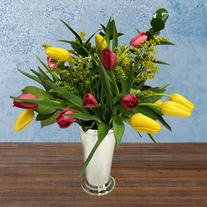 Bouquet of yellow and pink tulips in a tall silver container. 