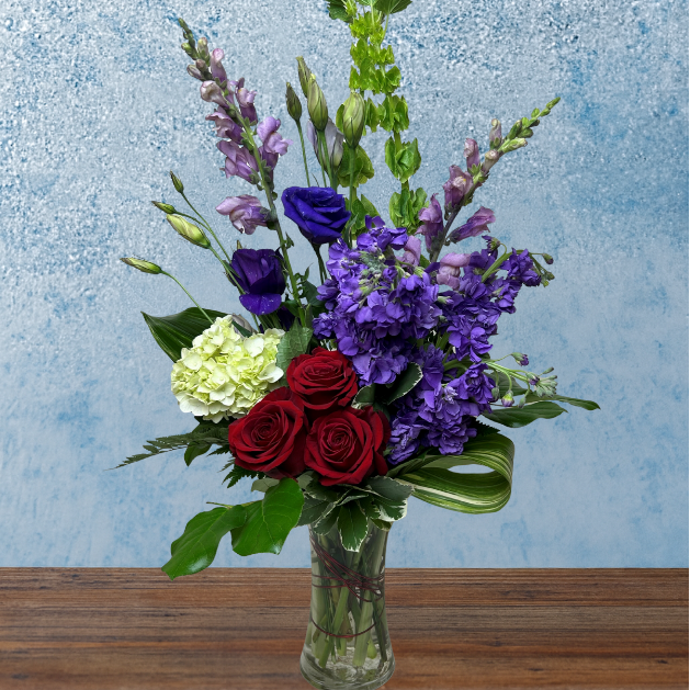 Tall purple bouquet. Flowers include lavender & purple stock, purple lisianthus, green bells of Ireland, white green Hydranea and 3 red roses 