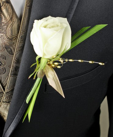 White rose boutonniere with greenery and gold ribbon and pearl accents on a black suit jacket.