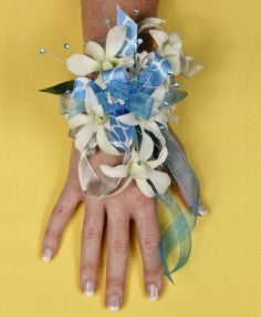 White orchid wrist corsage with blue and silver ribbons, pearl accents, and greenery, perfect for proms or weddings.