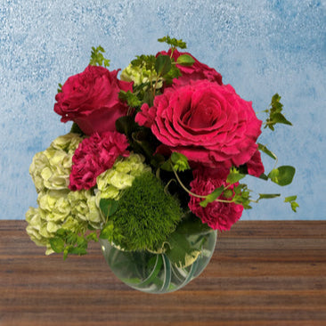 Floral arrangement in a bubble bowl. Included in the arrangement are vibrant pink roses and green hydrangea.
